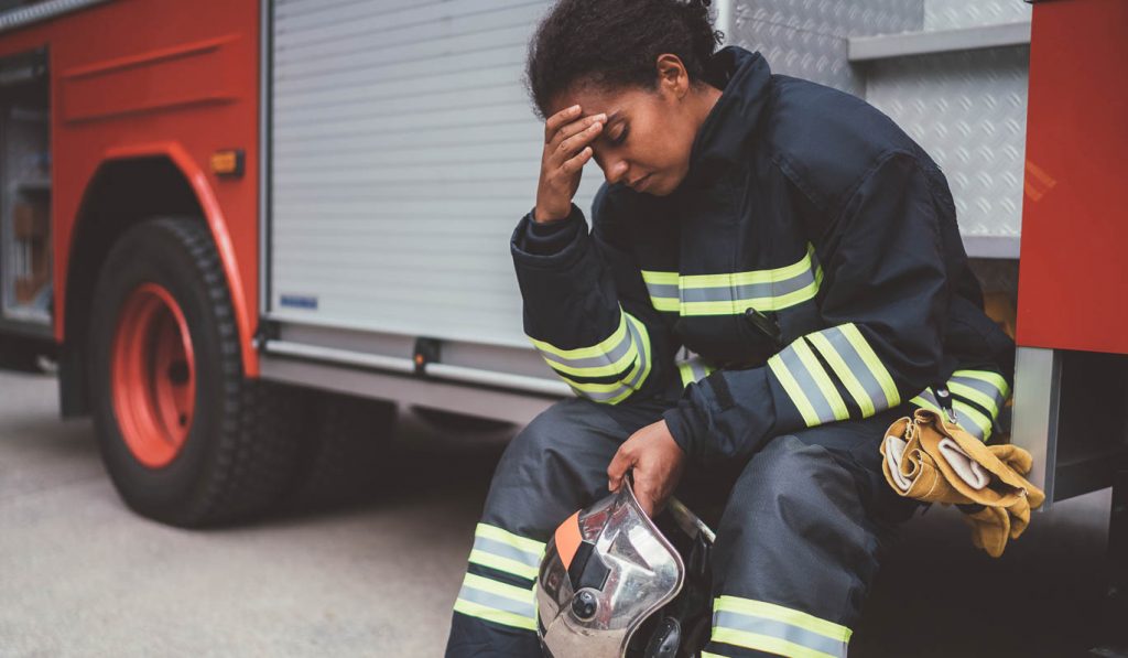 image of firefighter sitting on firetruck, hand to forehead